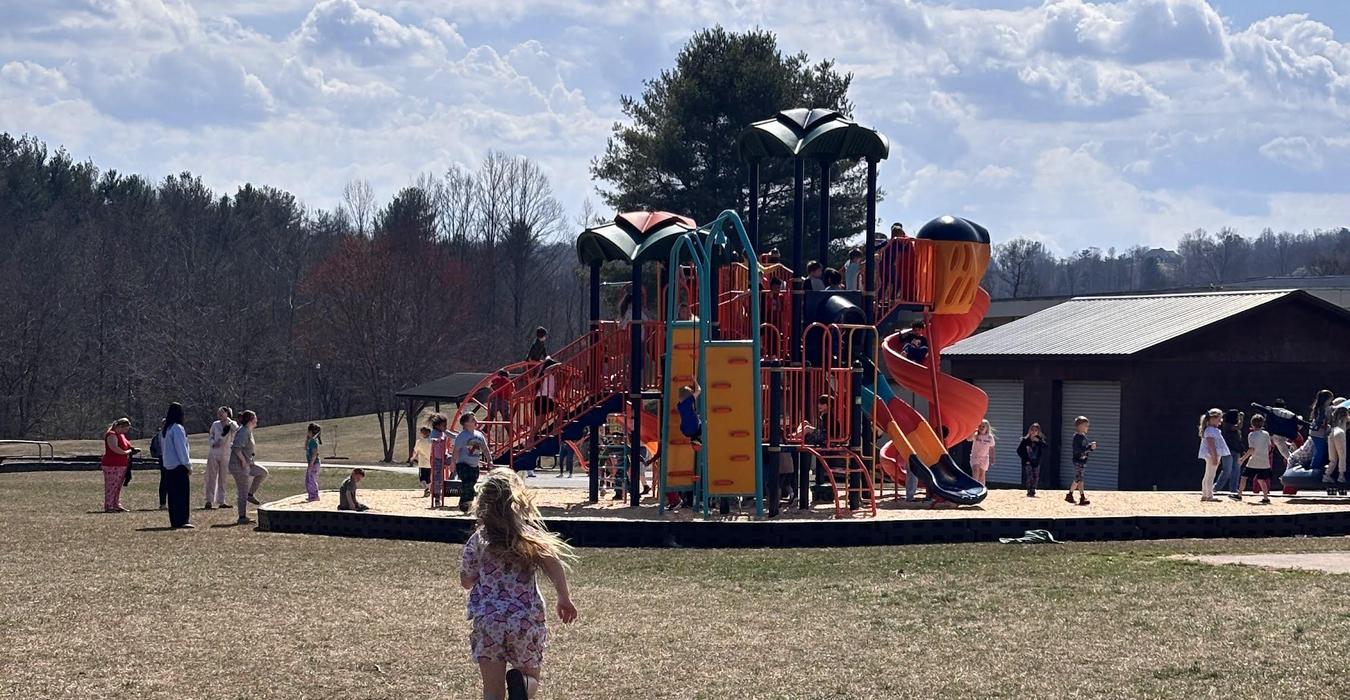 A child running towards a lively playground filled with children playing.