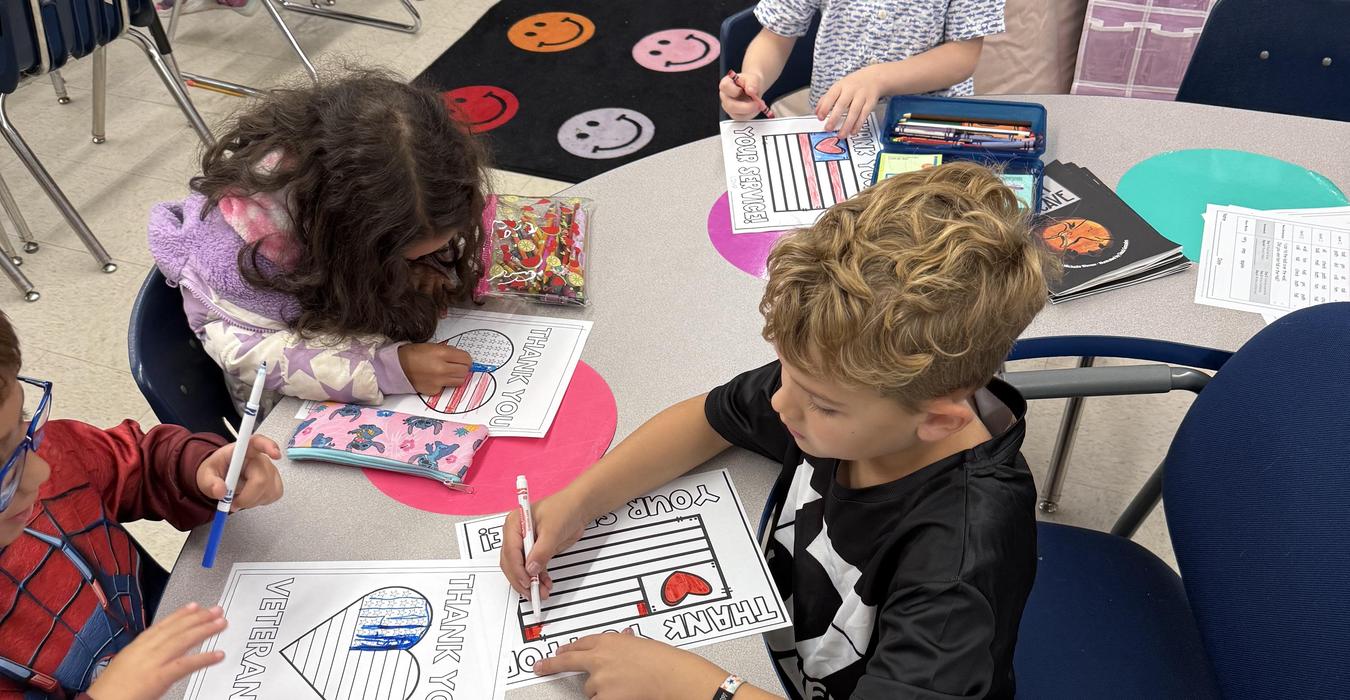 Children coloring thank you cards for Veterans at a classroom table.