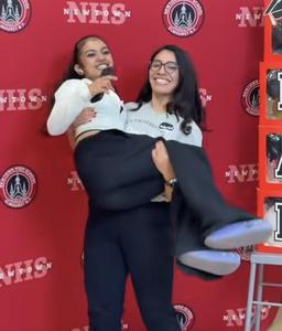 a student picking up another in front of a backdrop