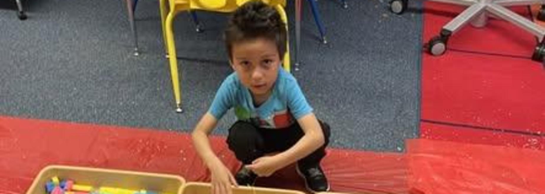 A child playing with three sensory bins filled with different textures and colors.
