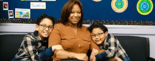 A woman with two boys seated on a couch, smiling at the camera.