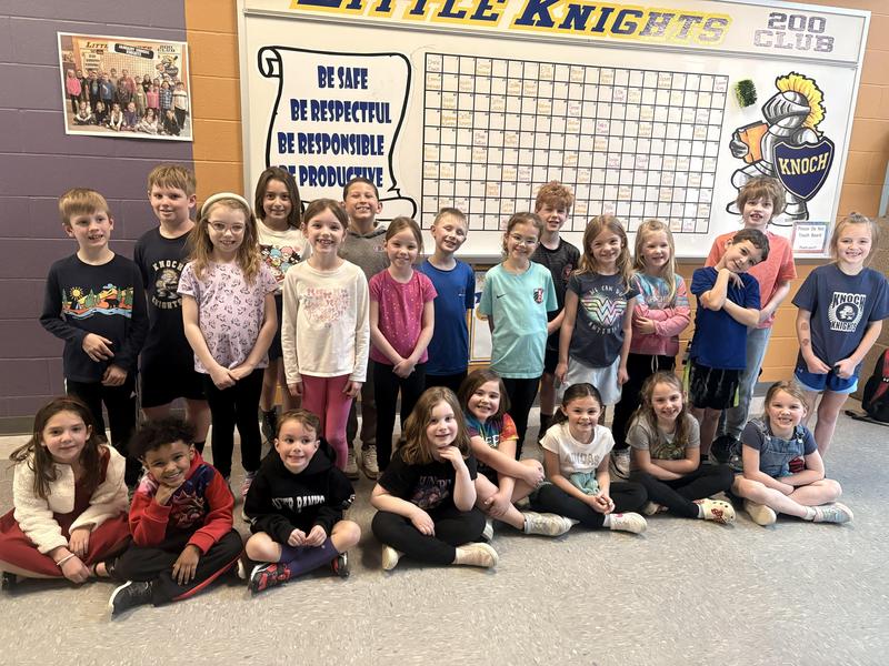 students seated and standing in front of 4 B's board