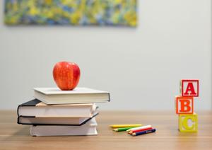 An apple sits on a stack of books next to colorful pencils and building blocks.