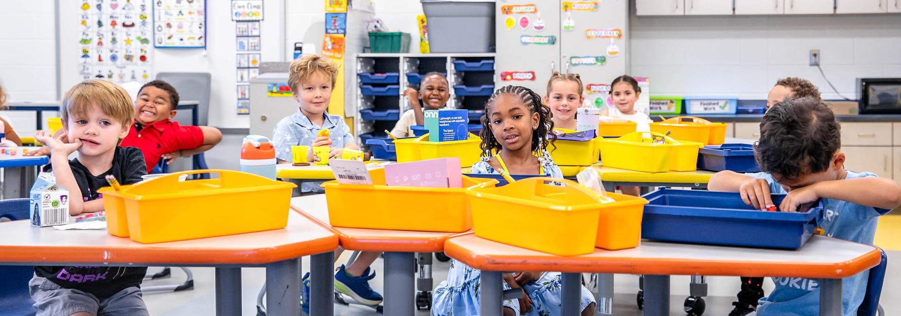 Students sitting at desks with yellow bins in a bright classroom.