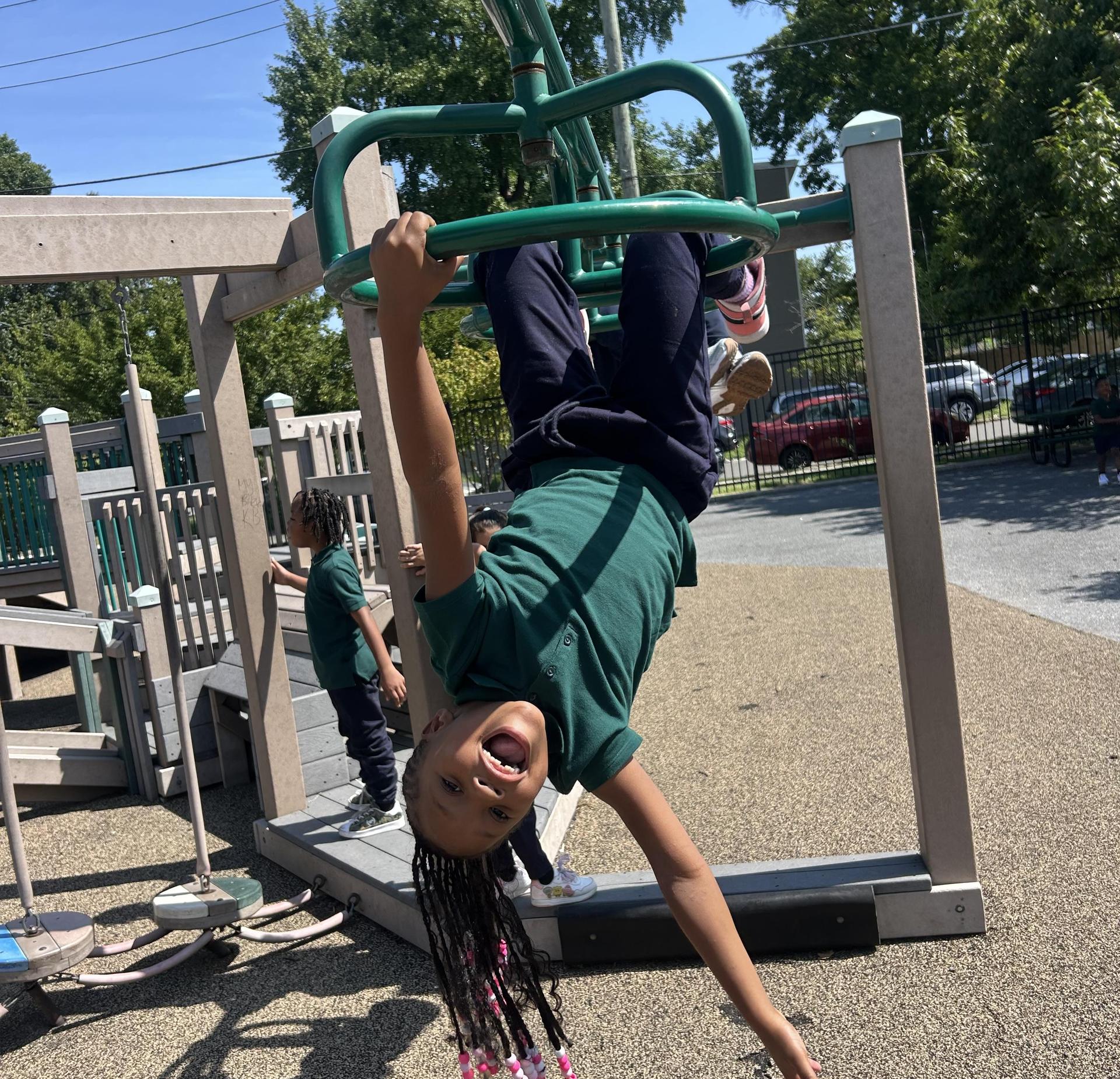 Child hanging upside down on playground equipment, smiling joyfully.