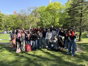 A large group of diverse people gathered outdoors in a sunny park setting.