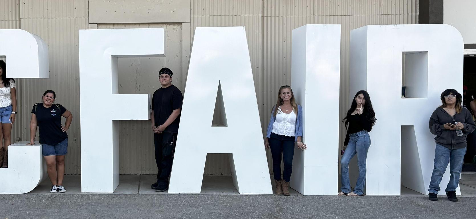 Group of six people posing by large white letters spelling 'KC FAIR'.