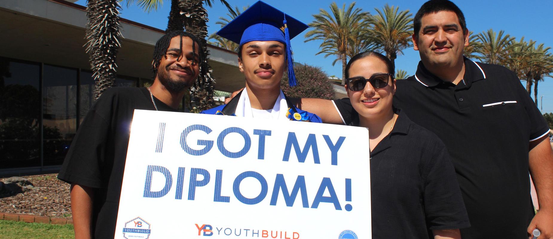 Graduate Miguel poses with his family and a sign that says "I got my diploma!"
