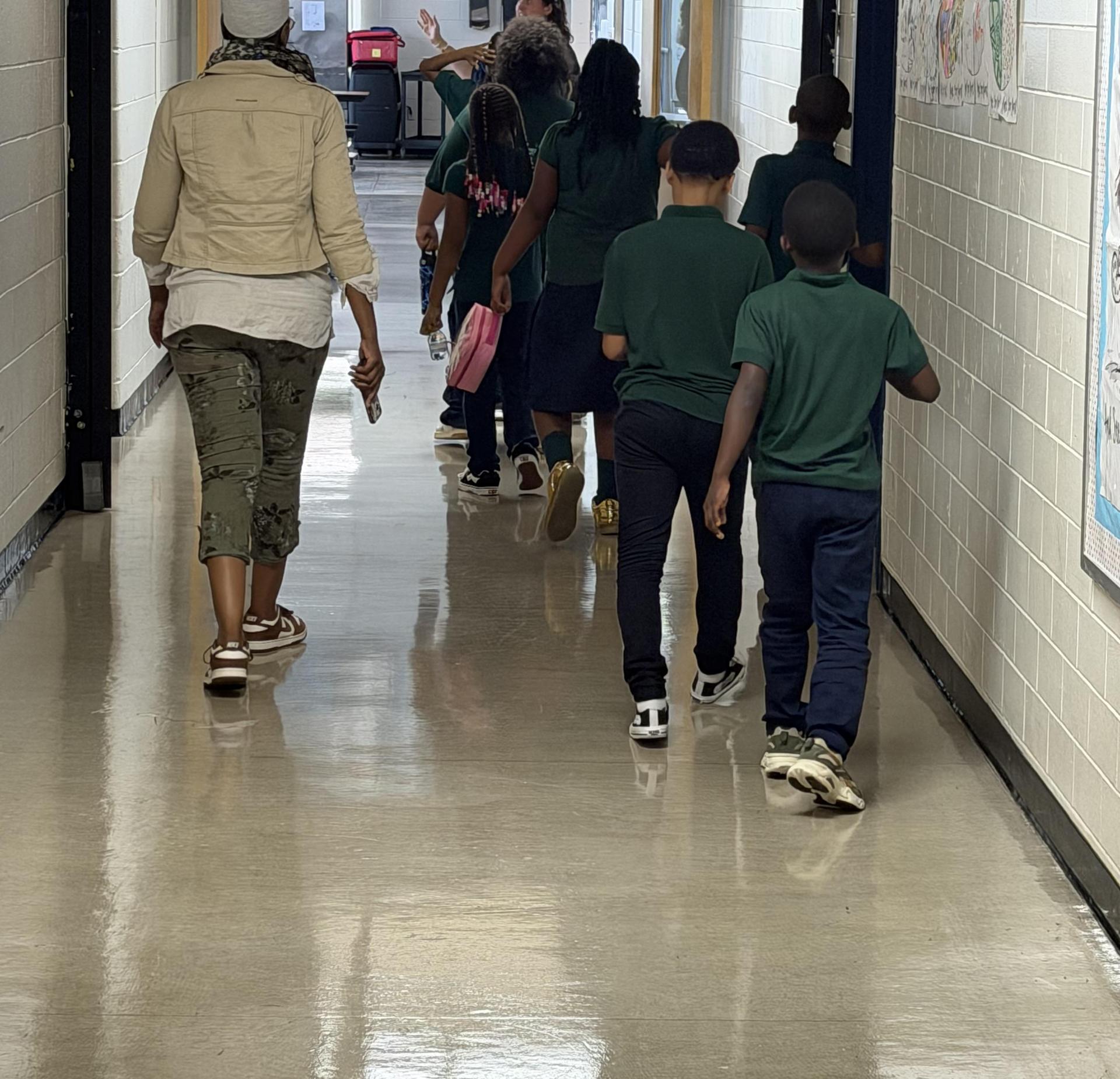 A group of children and an adult walking down a school hallway.