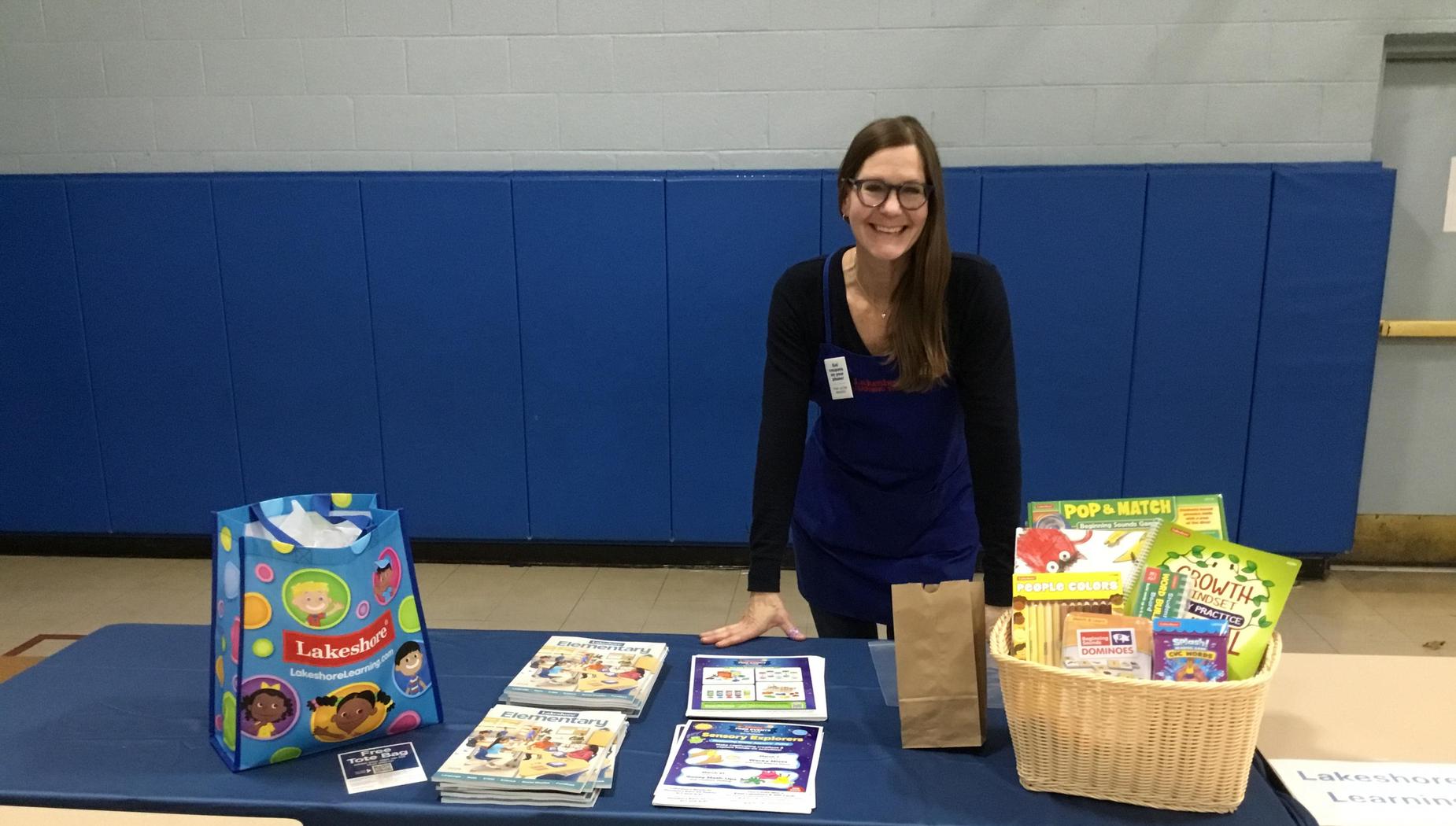 A woman at a table displaying educational materials and games at a community event.
