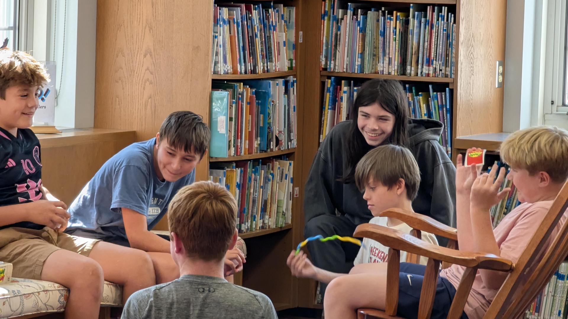 Group of children sitting in a library, engaging and laughing together.