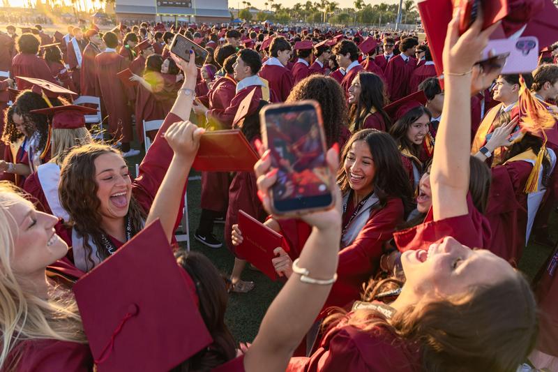 A group of graduates celebrate their milestone achievement by raising their hands and cheering in a circle.