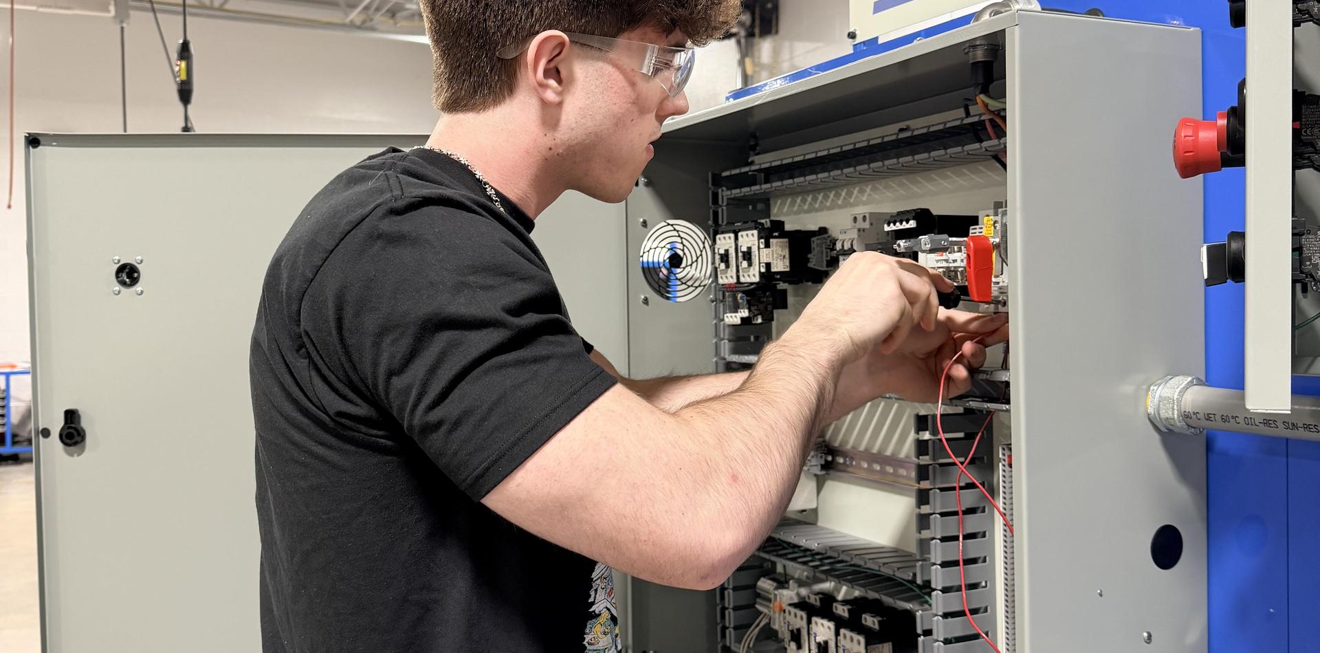 A student works on wiring inside an electrical control panel.