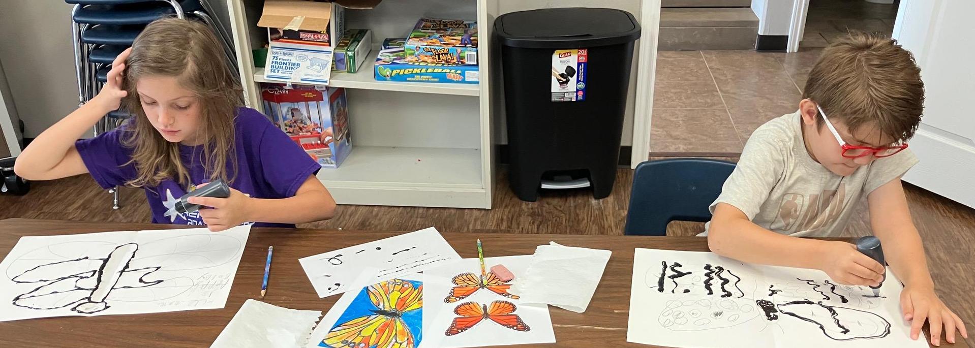 Two children working on art projects with illustrations of insects on the table.
