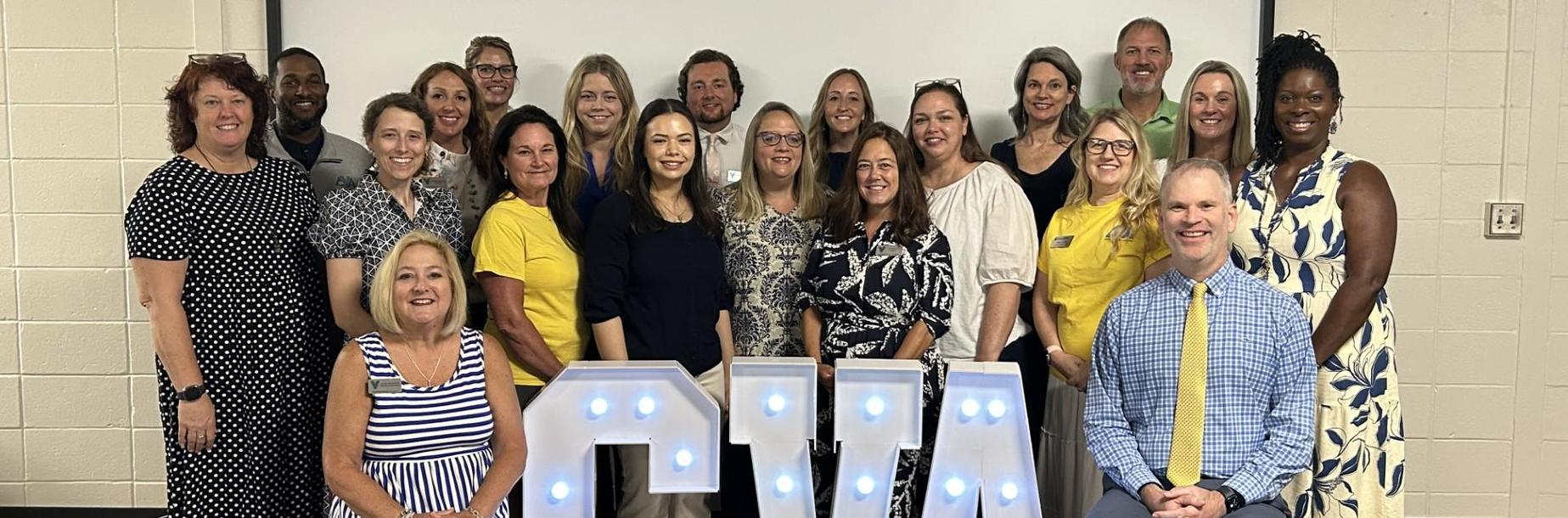 A diverse group of people posing together in front of large illuminated letters spelling 'CVA'.