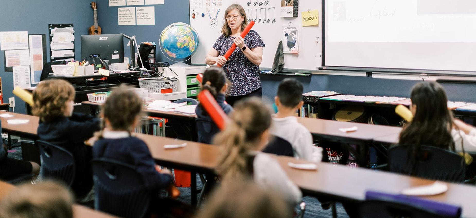 Music teacher leads elementary students in a rhythm lesson with boomwhackers