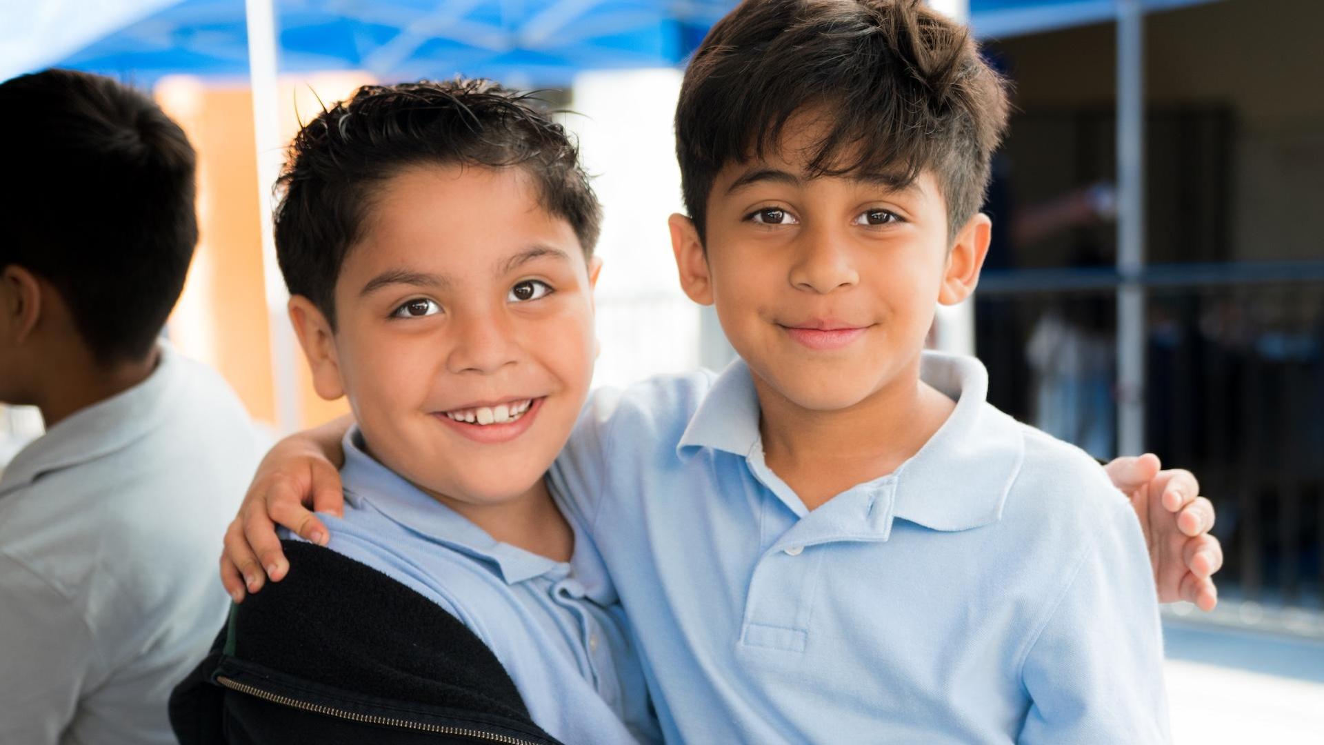 Two boys smiling and hugging each other in a casual setting.