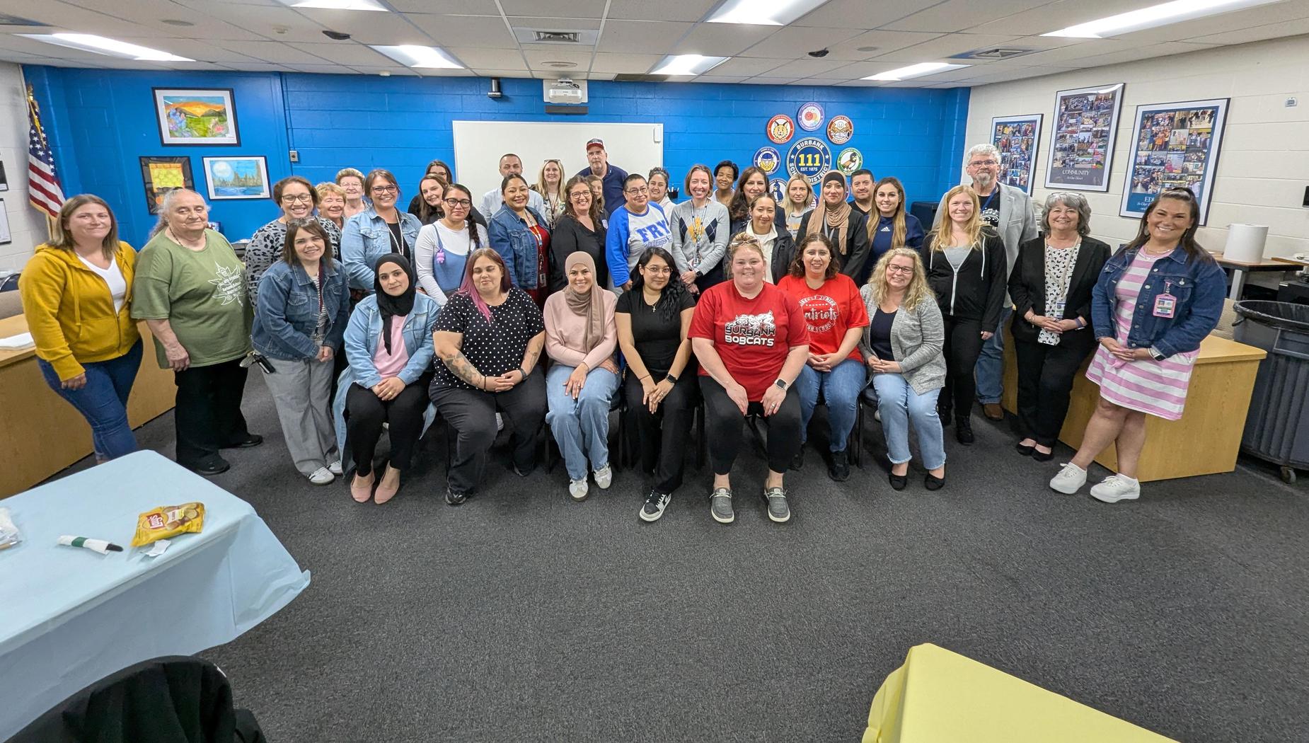 A large group of people posing together in a classroom setting.