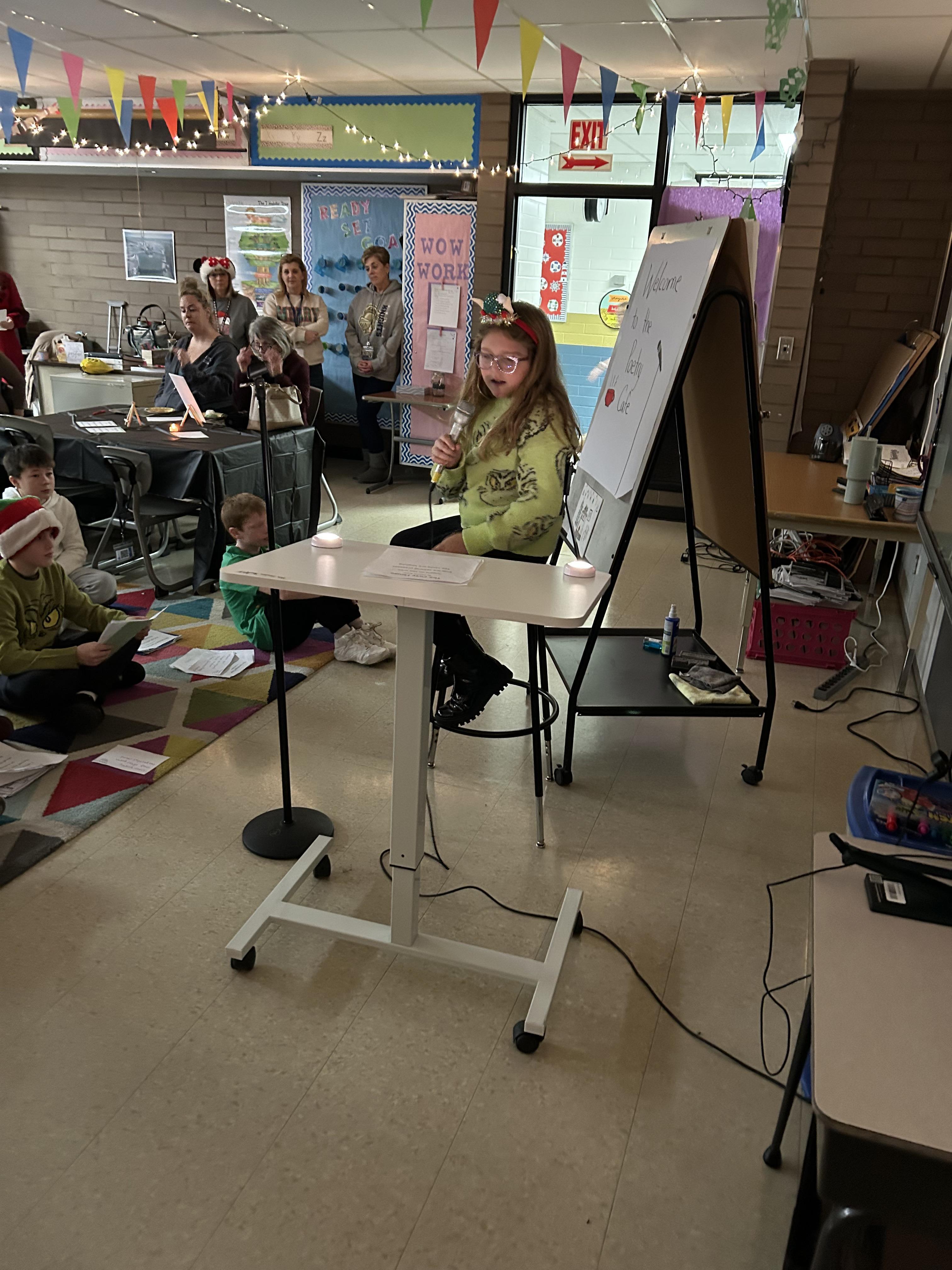 student reading poem in dim lit room with family watching