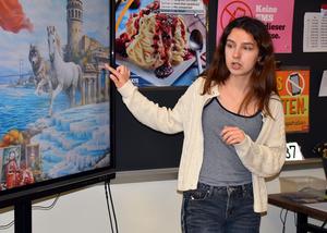A student points at a colorful mural displayed on a screen during a presentation.