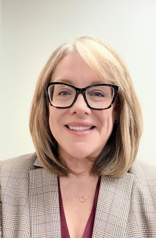 Headshot of Amy Coleman smiling, wearing glasses and a blazer against a light background.