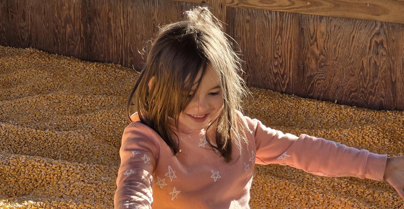 Child joyfully sitting in a large pile of corn kernels.