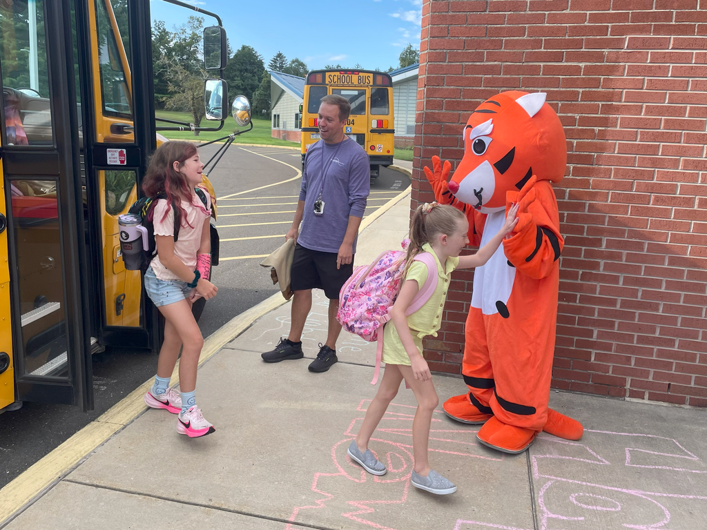Mr. Blocher and the mascot, Stripes, greeting students as they arrive off of the bus.