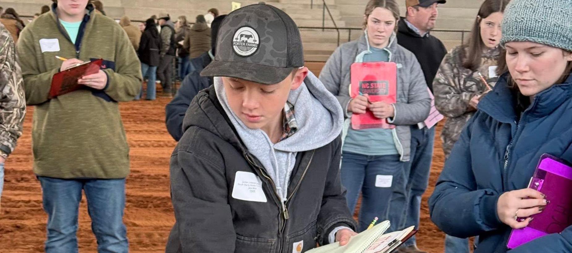 A person evaluating sheep in a barn setting, with attendees nearby.