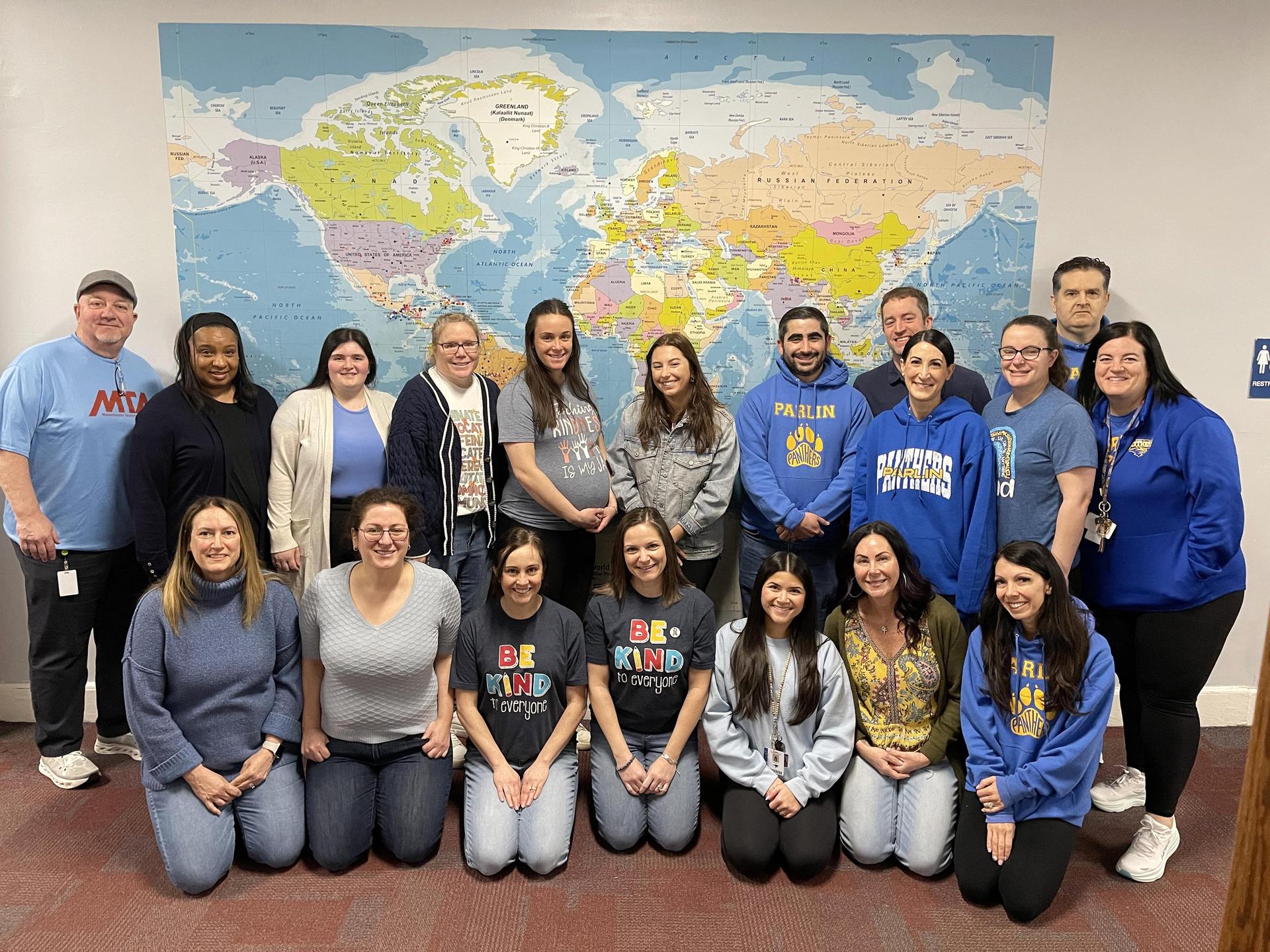 Large group of staff members posing in front of a world map.