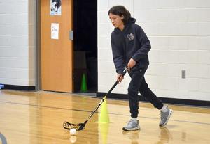 A student playing ball hockey in a gymnasium