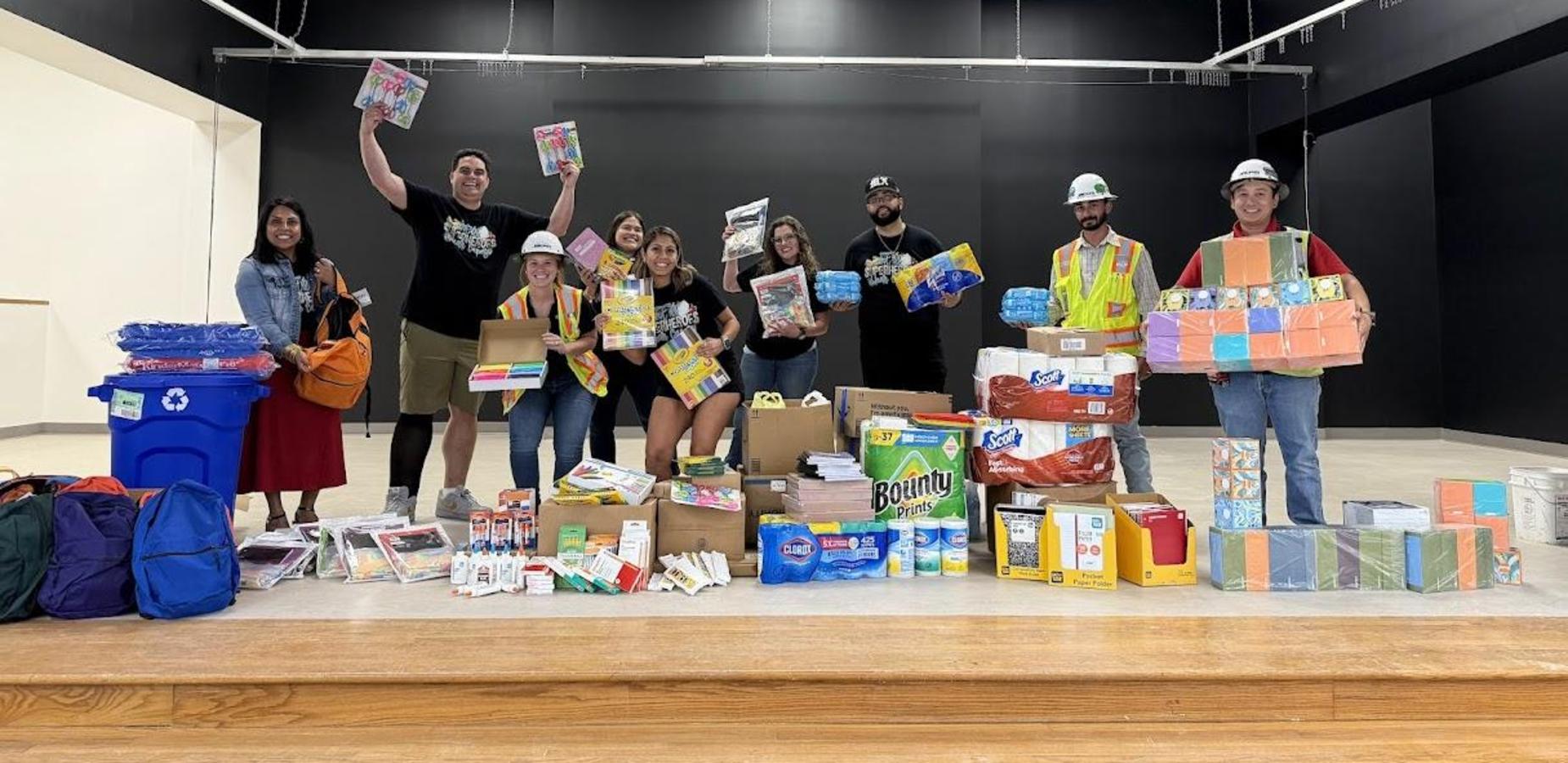 Staff and construction workers standing with school supplies on stage