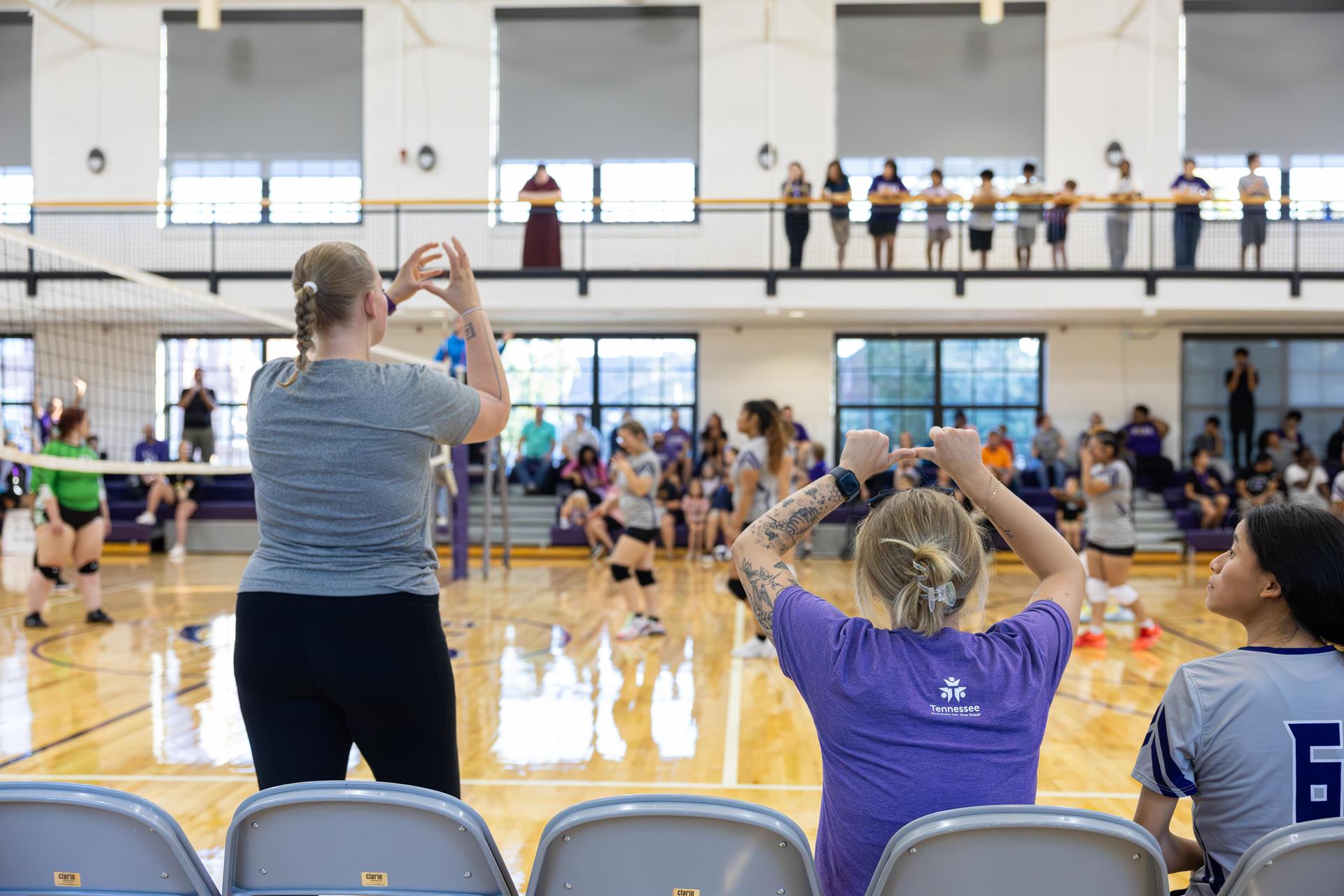 Fans and players cheering during a volleyball match in a gym.
