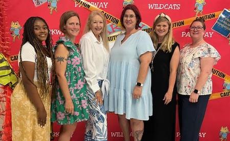 Women posed together in front of a caution-themed backdrop with a wildcat mascot.