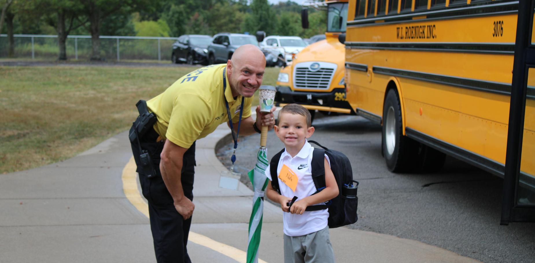 Smiling school resource officer with a young boy holding a backpack and smiling.