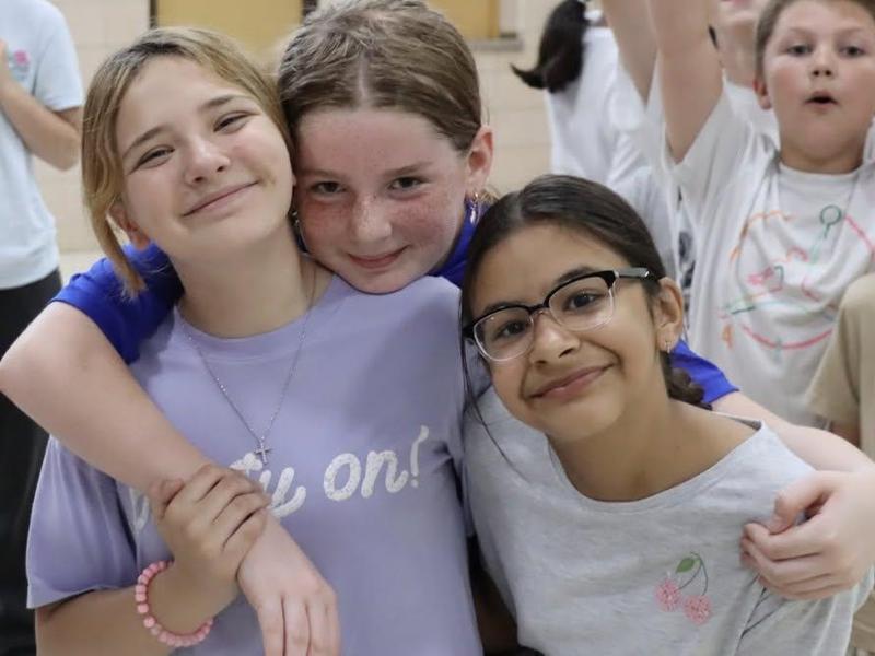 Three smiling girls embrace, each showing joy and friendship.