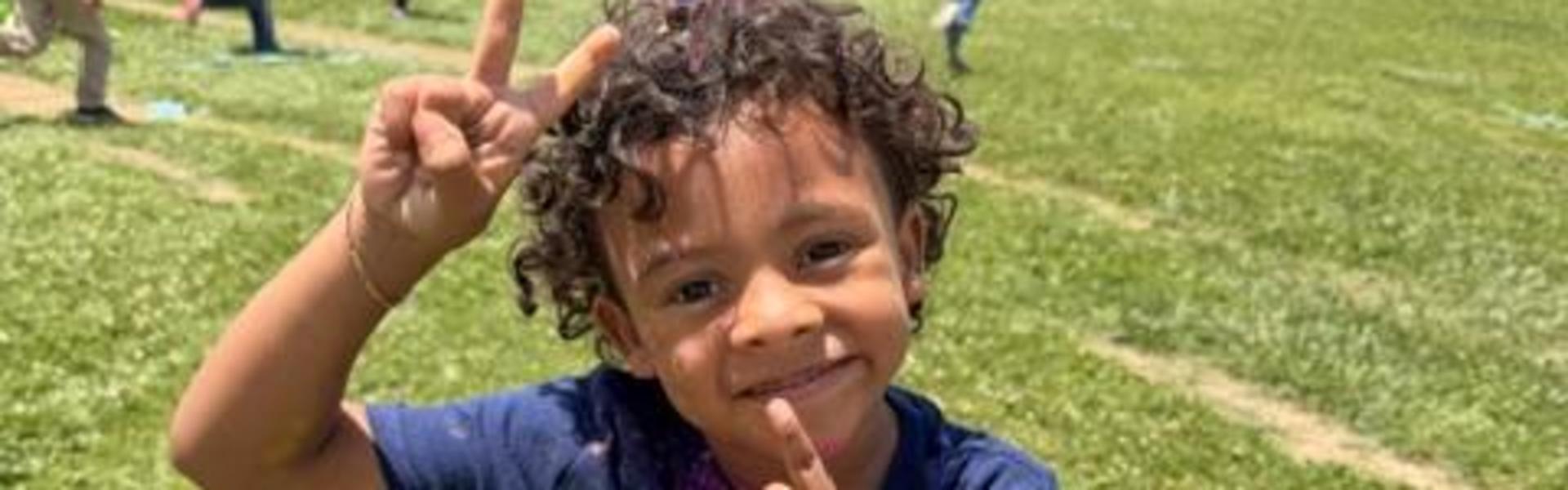 Child with a finger on their chin, wearing a colorful shirt and smiling.