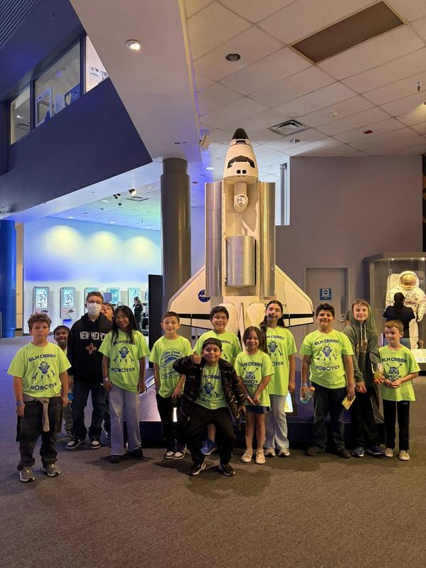 students in neon green shirts standing in front of rocket