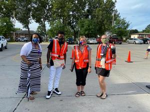 Image shows four adults wearing masks and safety vests, ready to screen scholars