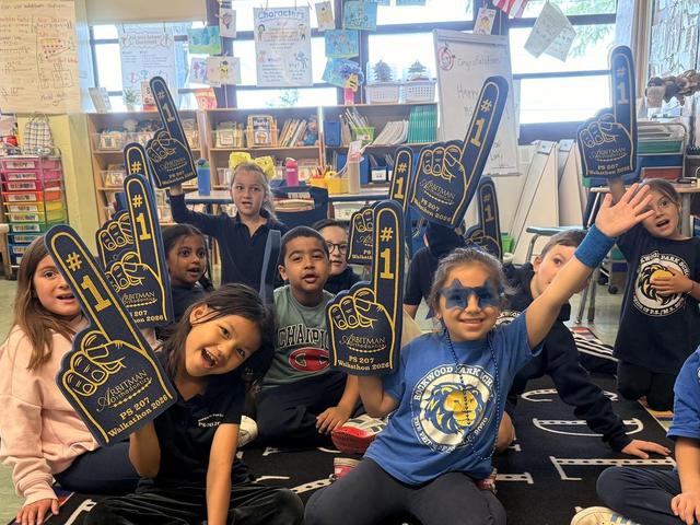 Students holding foam fingers, celebrating and smiling in a classroom.