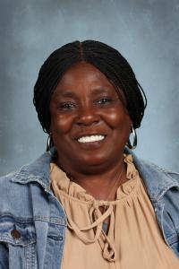 Smiling woman with braided hair in a denim jacket against a gray background.