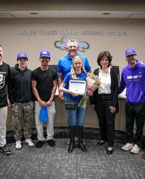 A student receives an award surrounded by school staff and peers, all smiling.