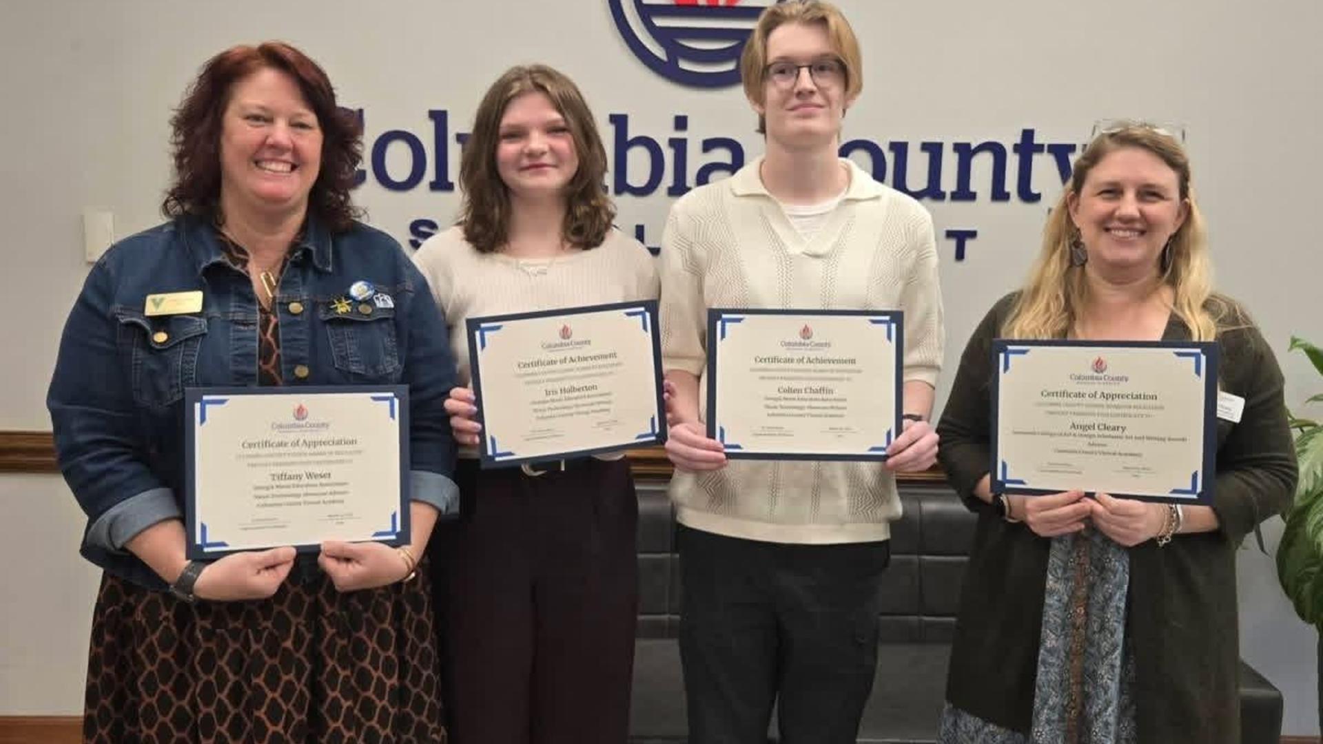 Four individuals holding certificates in front of a Columbia County backdrop.