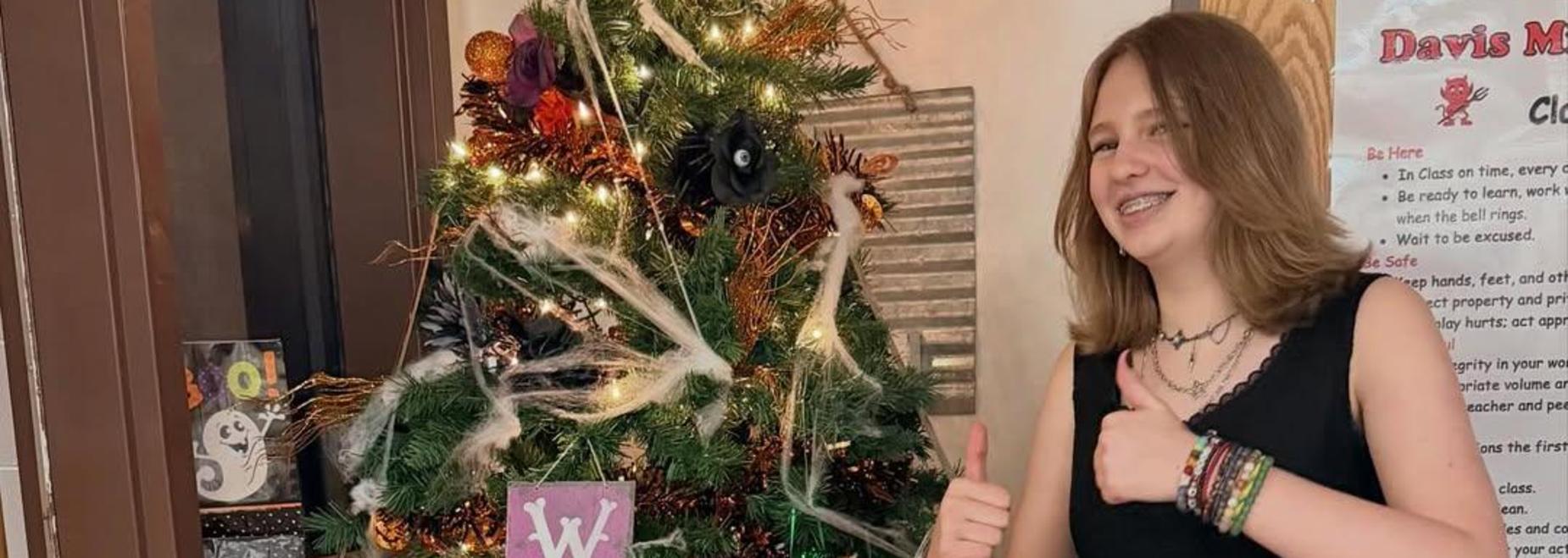 A girl standing next to a decorated Halloween tree with pumpkins and a welcome sign.