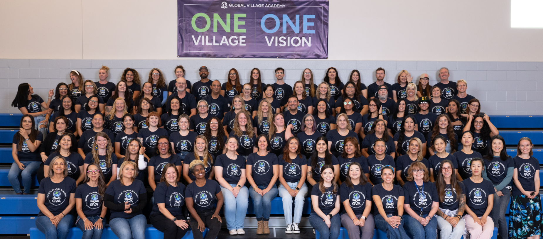 Group photo of many people in matching shirts, standing together in a school gymnasium.