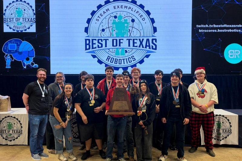 Robotics students standing with trphy in front of Best of Texas Robotics sign