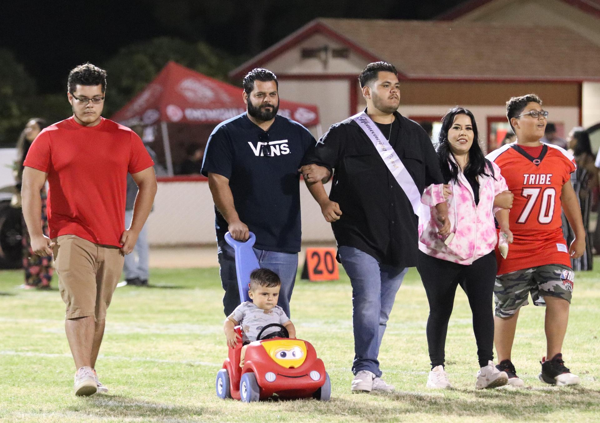 homecoming king and queen candidates walking across the field with their escorts