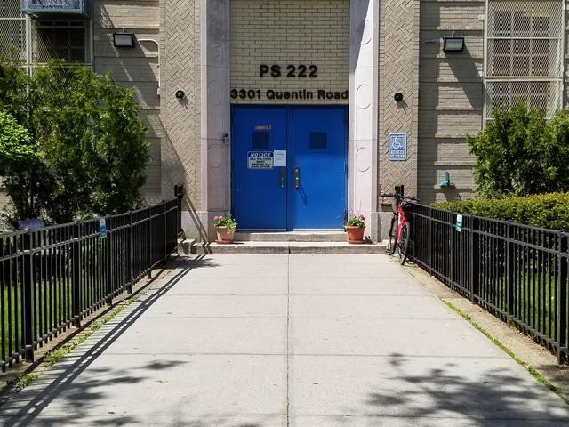 Entrance of PS 222 on Quentin Road with a blue door and fenced pathway.