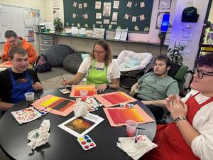 Students creating art together at a classroom table with paint supplies.