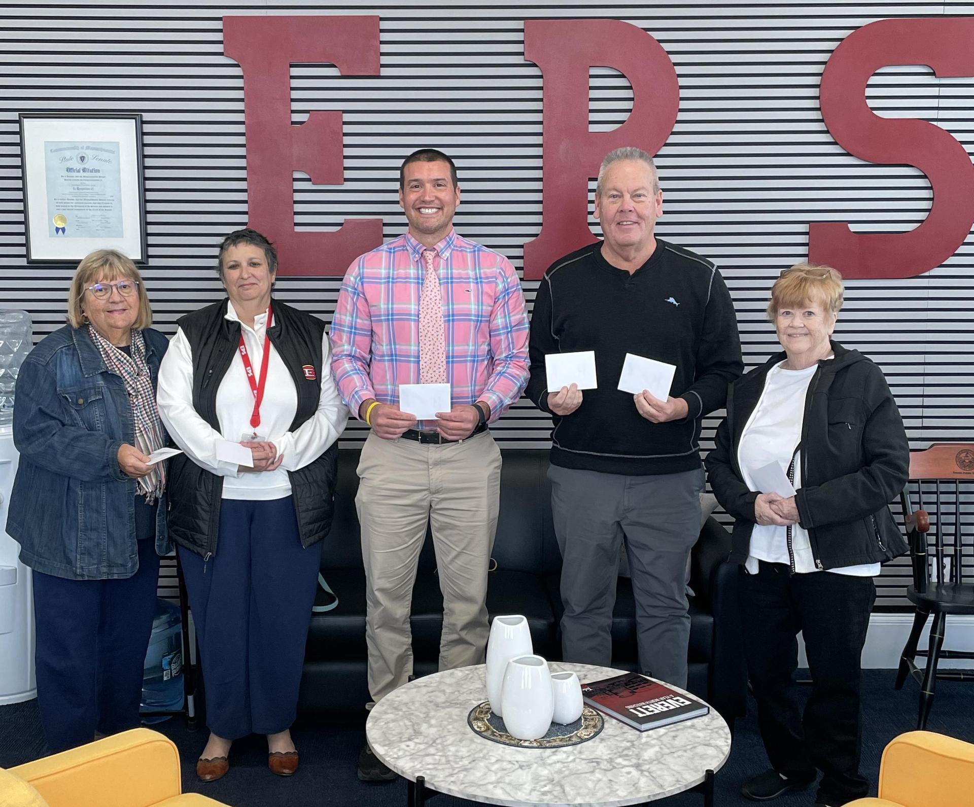 Five people standing together, holding cards in a modern indoor setting.