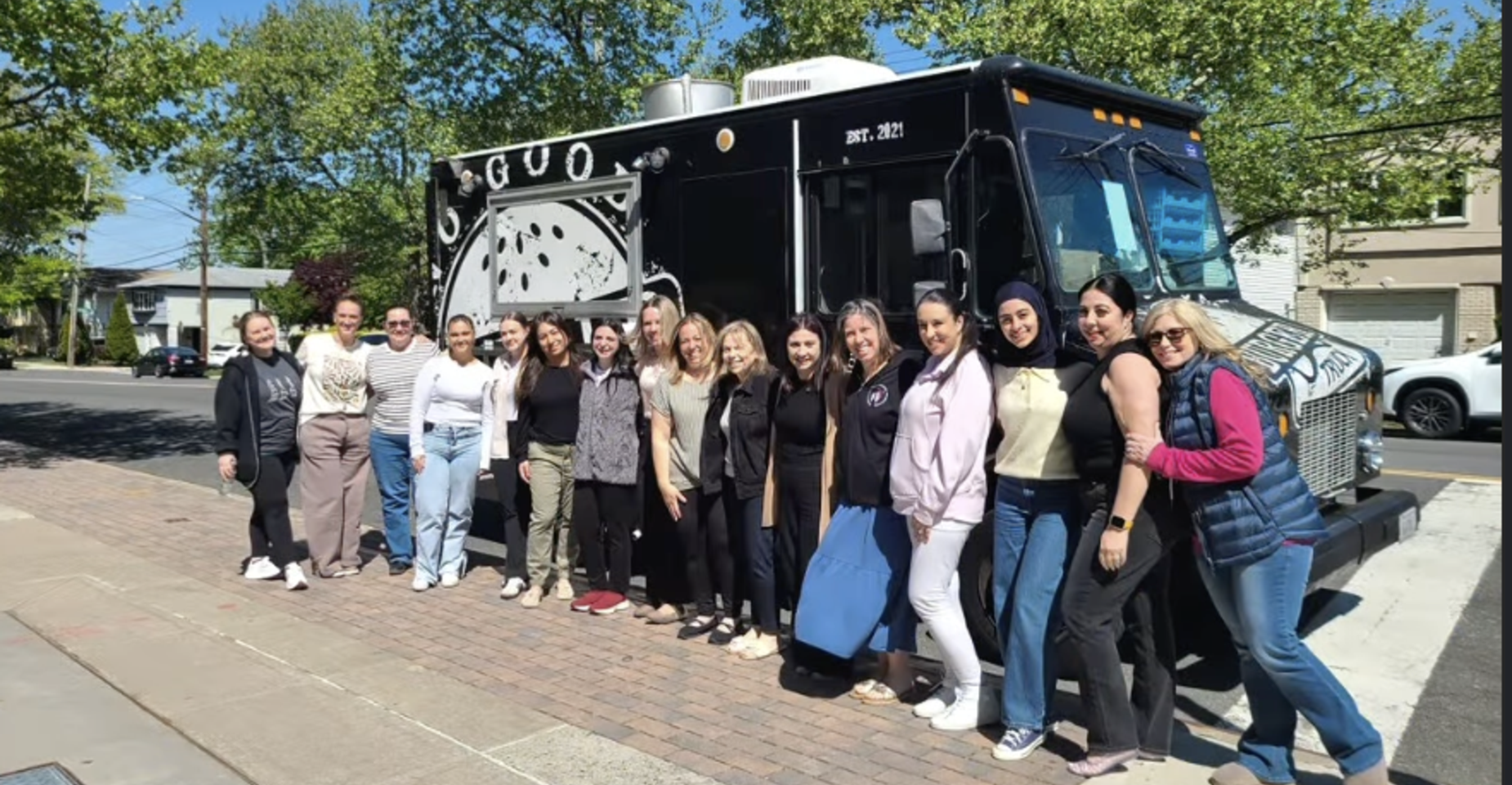 Group of people standing in front of a food truck, smiling together.
